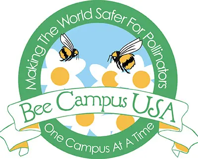 Logo for Bee Campus USA featuring two bees flying over white flowers with yellow centers. Surrounding text reads, "Making the World Safer for Pollinators" and "One Campus at a Time.