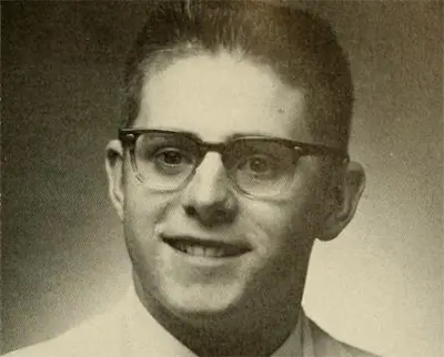 A vintage black-and-white portrait of a young person wearing glasses and a collared shirt. The individual is smiling, and the photo has a classic, formal tone typical of old yearbook or school pictures.