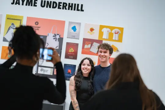 Two students in front of a graphic design display at a gallery