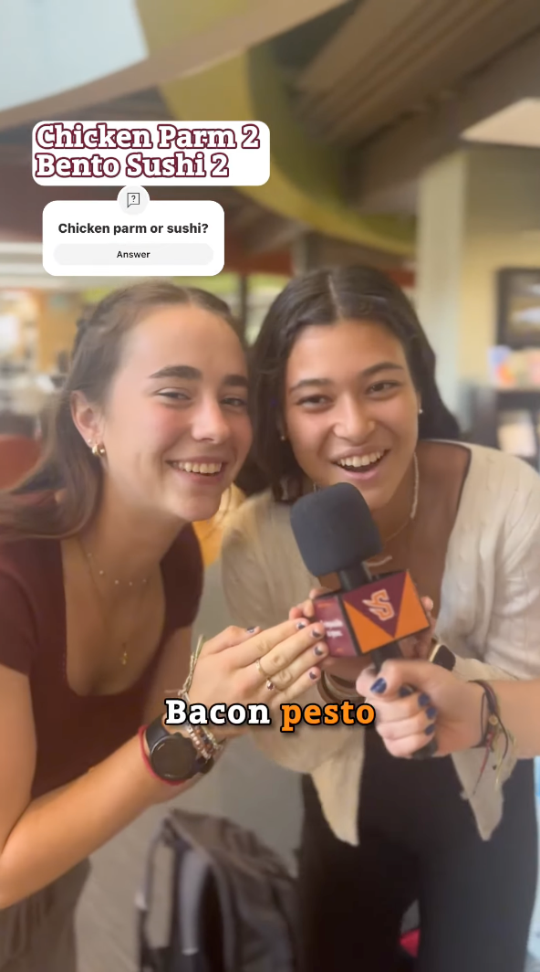 Two people smiling and holding a microphone indoors seem to capture the essence of living on campus. The on-screen text reads, "Chicken Parm 2 Bento Sushi 2" and "Bacon pesto," with a question above: "Chicken parm or sushi?" A bustling cafeteria setting blurs in the background.